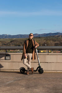 Young man smiling enjoying the sunny day in winter time with a hot coffee and an electric scooter