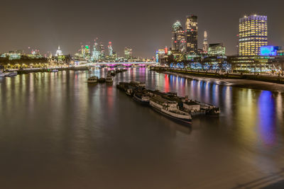 Illuminated city by river against sky at night