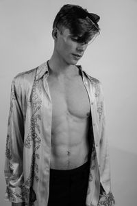 Man wearing fully unbuttoned shirt while standing against wall