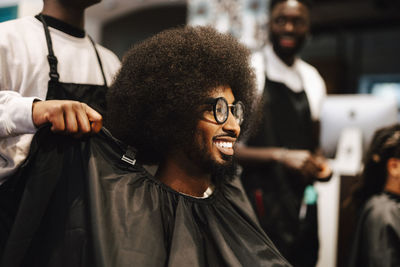 Cropped image of barber putting apron to male customer in salon