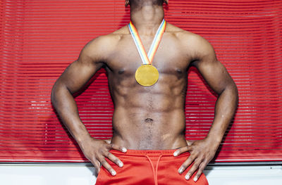 Unrecognizable shirtless african american man with fake medal standing against red wall during party