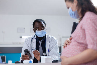 Doctor wearing mask prescribing medicine to pregnant woman