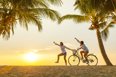 Friends with bicycle gesturing at beach against sky