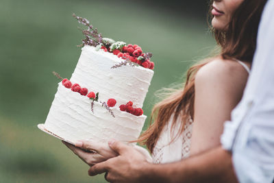 Midsection of couple holding wedding cake at farm