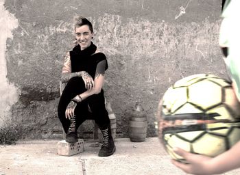 Portrait of young woman sitting against wall