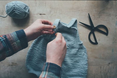 High angle view of hand sewing buttons on knitted baby cloth