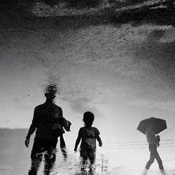 People standing on wet beach against sky