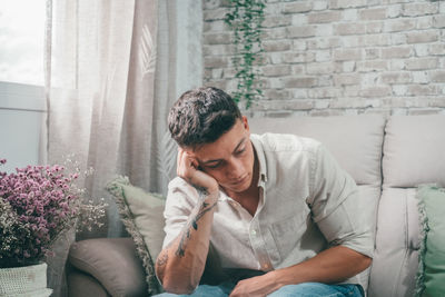 Side view of young man using mobile phone while sitting on sofa at home