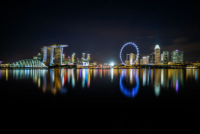 Illuminated buildings by river against sky at night