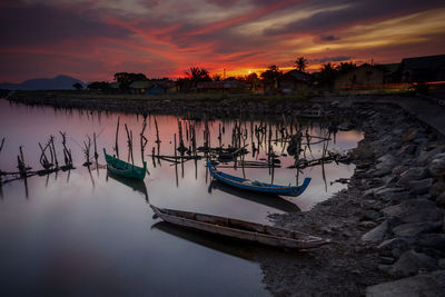 Fishing boats moored in lake against sky during sunset
