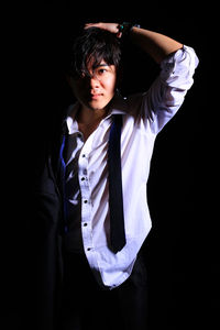 Portrait of young man standing against black background