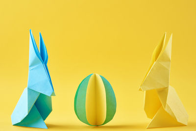 Two paper origami esater rabbits and colored egg on a yellow background. easter celebration concept