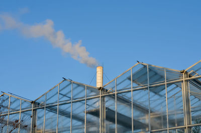 Low angle view of smoke emitting from factory against blue sky