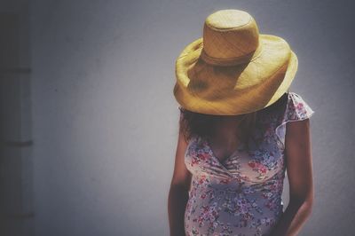 Pregnant woman wearing yellow hat standing against wall