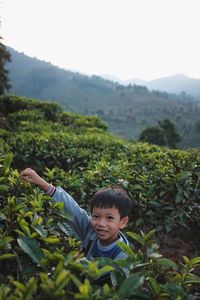 Portrait of boy standing amidst plants on mountain against clear sky