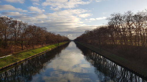Canal amidst bare trees against sky