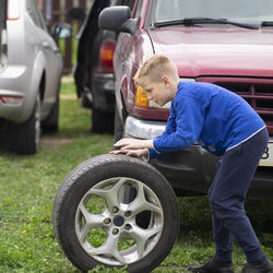 Side view full length of boy pushing tire on land