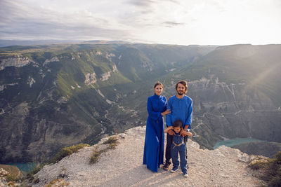 Family of three people stands on the mountain gorge during sunset in dagestan