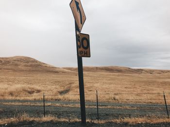 Road sign on field against sky