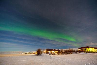 Illuminated buildings against sky at night with aurora during winter