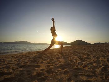Full length side view of woman practicing yoga on sand at beach during sunset
