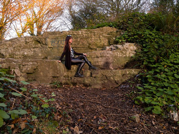 Young woman sitting on old wall in forest