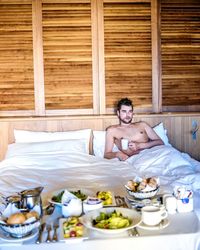 Shirtless man with coffee on bed at home
