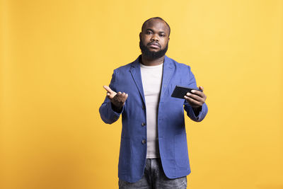 Portrait of young man standing against yellow background