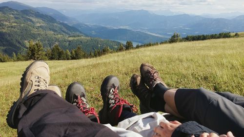 Low section of friends resting on grassy field at mountain