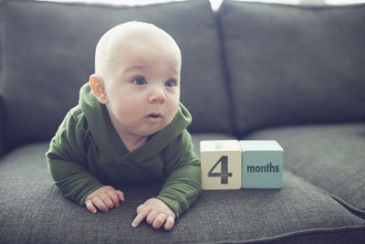 Baby boy looking away while lying by toy blocks on sofa at home