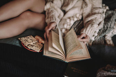Cropped young woman in a cozy knitted sweater reading a book on the bed. home aesthetics. winter 