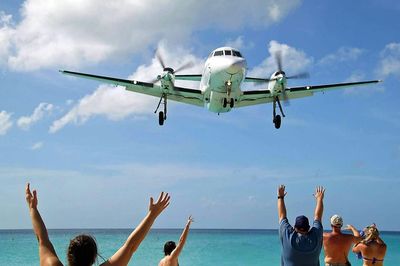 Rear view of people with arms raised looking at airplane flying over sea