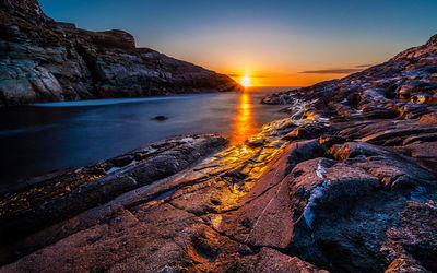 Scenic view of sea amidst rocks against sky during sunset