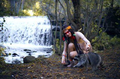 Young woman in traditional clothing with raccoon in forest