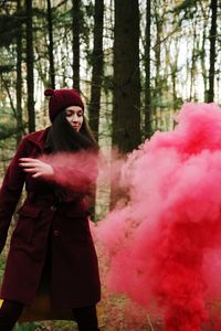 Woman standing by pink smoke against trees at forest