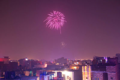 Firework display over illuminated city against sky at night