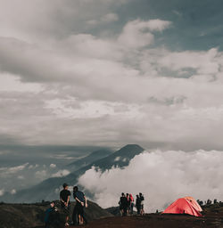 People walking on mountain against cloudy sky