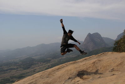 Excited young man jumping at mountain peak against sky