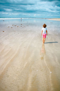 Rear view of girl wading in sea against sky