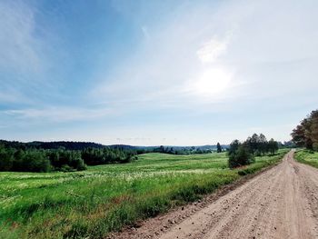 Dirt road amidst field against sky