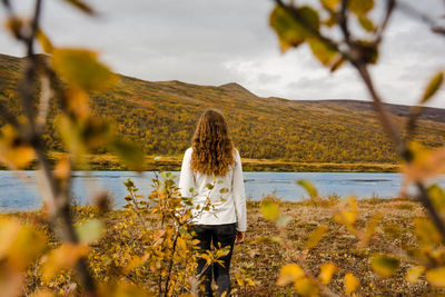 Rear view of woman standing by river against cloudy sky