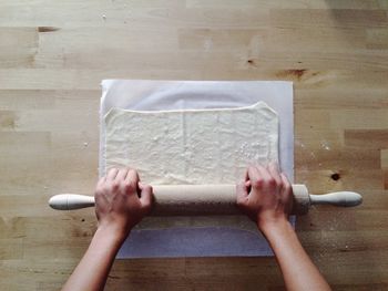 High angle view of cropped hands rolling dough in kitchen