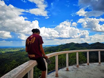 Rear view of man standing on railing against mountain