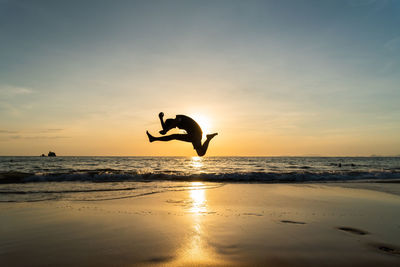 Silhouette man jumping on beach against sky during sunset