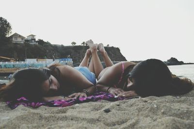 Friends lying on sandy beach against clear sky