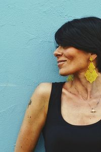 Mid adult woman wearing golden earrings by wall