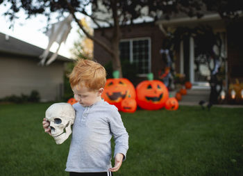 Toddler holding skeleton head in front of outdoor halloween decor