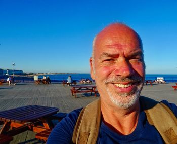 Portrait of smiling man standing at beach against blue sky