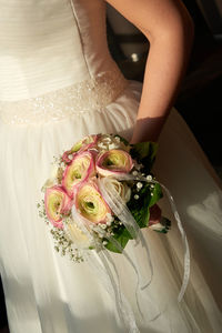 Midsection of bride holding flower bouquet while standing outdoors