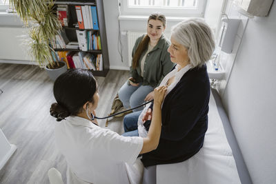 High angle view of female doctor listening heartbeat of senior patient in clinic